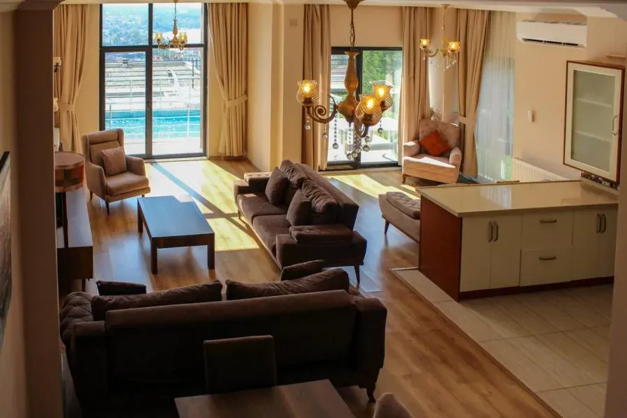 Yüksek tavanlı salon, koltuklar, mutfak tezgahı ve camın ardında havuz